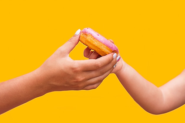 Female hand passes a pink delicious donut to a child's hand