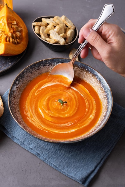 Mano femminile che prende la zuppa di crema vegana di zucca con un cucchiaio.