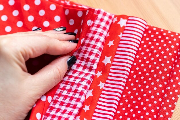 Female hand on a pile of five types of red and white cotton fabrics with different prints checkered ...