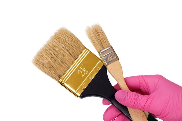 Female hand in a pink latex glove holding a house painter brushes on a white isolated background. Repair tool. Building tool. Close-up view.