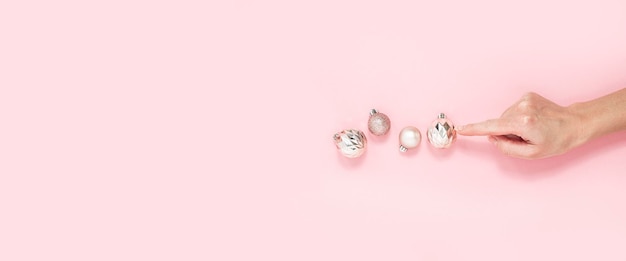 Female hand points to a single decorative balls on a pink background Top view flat lay Banner