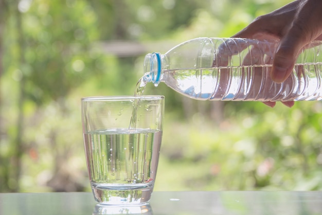 女性の手は、自然の背景でガラスに瓶から水を注ぐ