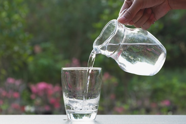 自然の背景でガラスに瓶から水を注ぐ女性の手