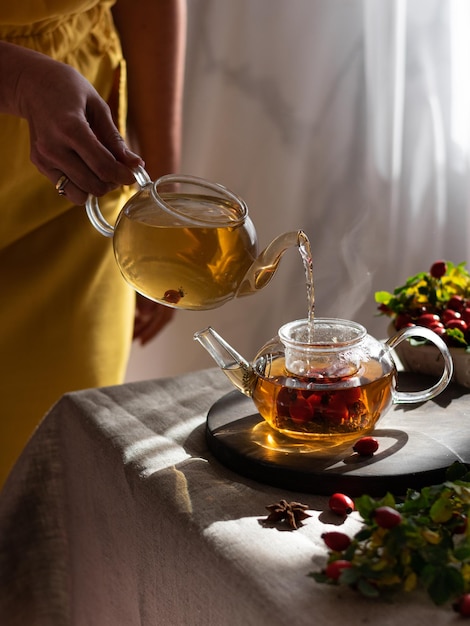 Female hand pours hot herbal tea into a glass mug Vertical