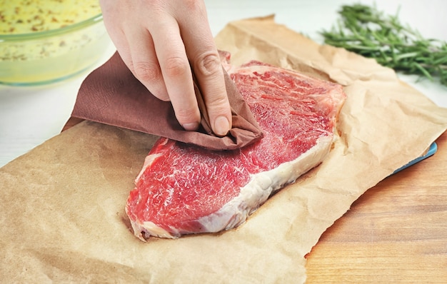 Female hand preparing raw steak on wooden board with parchment