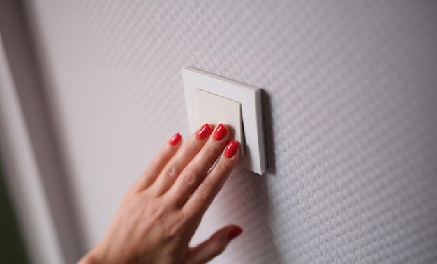 女性の手は灰色の壁のクローズアップで白いスイッチを押します