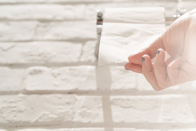 Foto la mano femminile che tira una carta velina bianca dal tessuto rotola nel bagno.