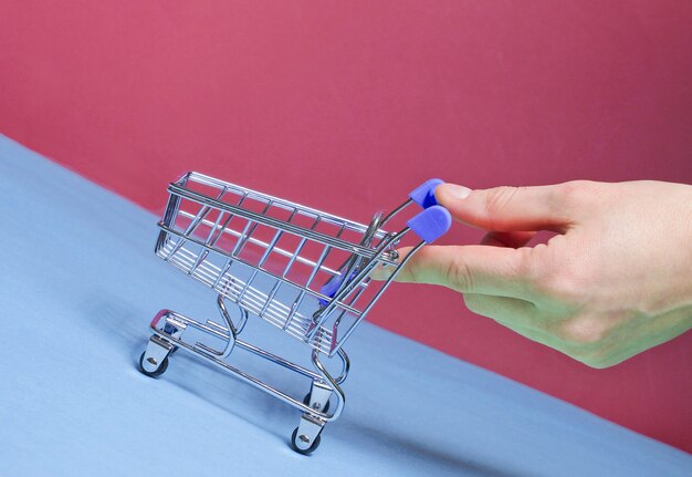 Foto la mano femminile spinge verso l'alto il mini carrello della spesa vuoto inclinato. concetto di acquisto, consegna