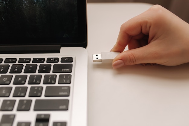 Female hand put USB adapter to copy file by laptop.