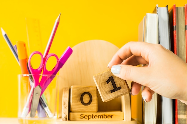 女性の手が木製のカレンダーに9月1日の日付の立方体を置きます