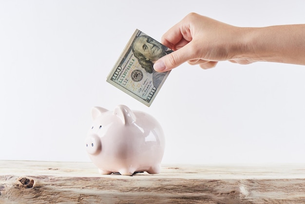 Female hand puts dollars in a piggy bank on a white background