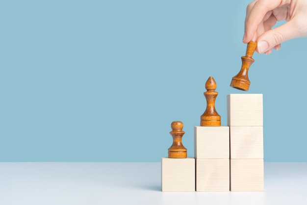 The female hand puts the queens figure on the top of the pyramid of wooden cubes The concept of career growth and development