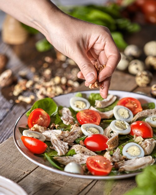 Female hand puts walnuts to the plate of freshly cooked salad from natural ingredients on a wooden