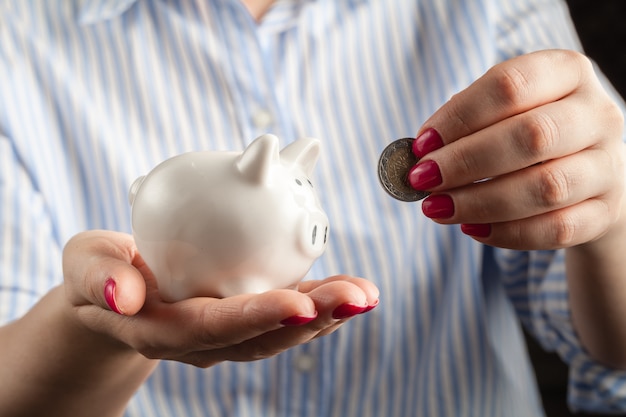 Female hand putting coin into piggy bank closeup