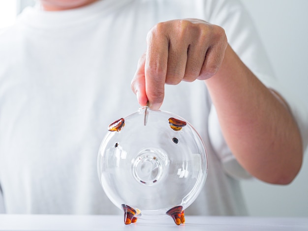 Female hand putting coin into piggy bank on white table closeup