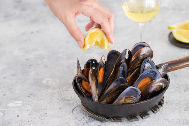 Female hand putting lemon on Steamed mussels served in frying pan.