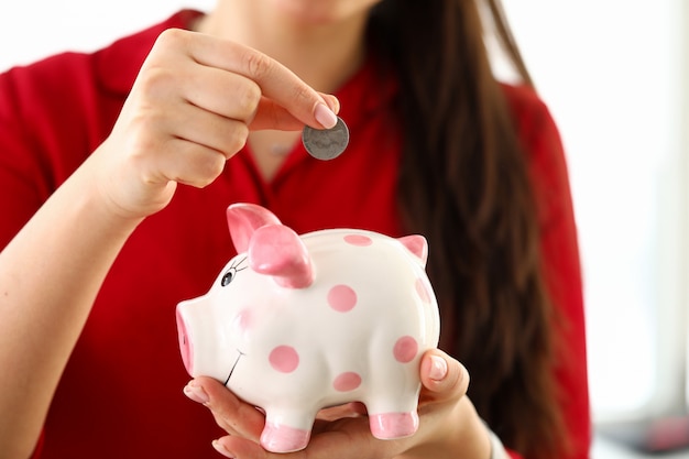 Female hand putting silver quarter into funny piggybank slot close-up