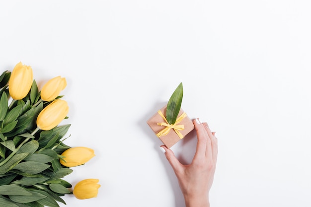 Female hand putting on the table a small box with a gift near the tulips