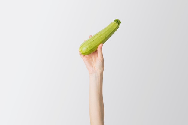 Female hand raised up fresh zucchini on a white background