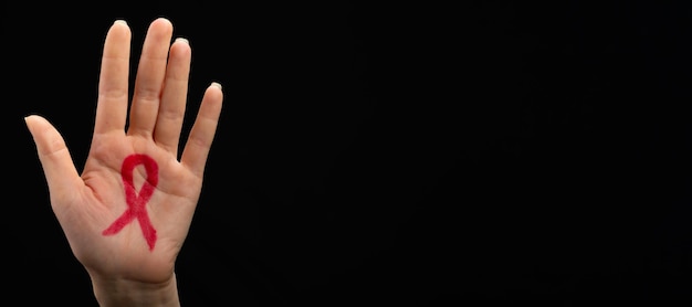 A female hand reaches up with a red awareness ribbon drawn on the palm. Black background. World AIDS day concept