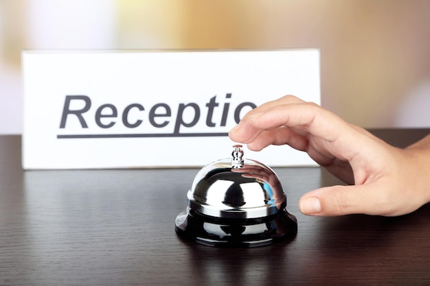 Foto campanello a mano femminile sulla reception dell'hotel su sfondo luminoso