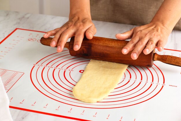 Pizza arrotolata a mano femminile o pasta di pane con un mattarello su un tavolo bianco, cosparsa di farina. cuocere passo dopo passo in cucina