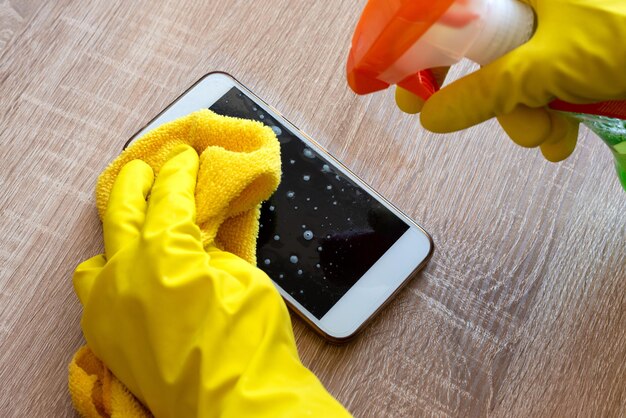 Female hand in rubber protective glove with rag wiping
smartphone using cleaning spray