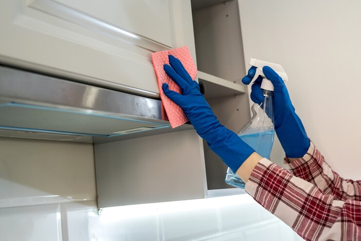 Photo female hand in rubber protective ñleaning cooker hood with rag in kitchen.