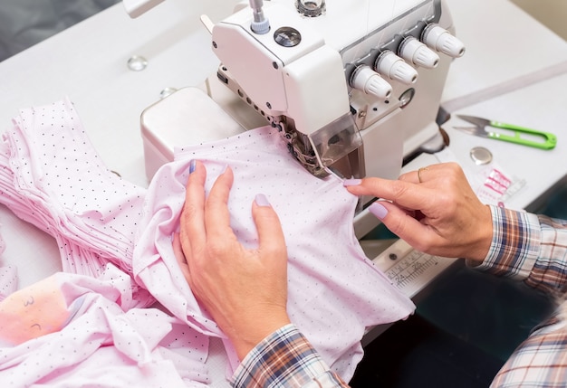 オーバーロック機でベビー服を縫う女性の手、服の製造