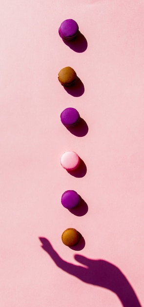 Female hand shadow abstract holding macarons on pink surface