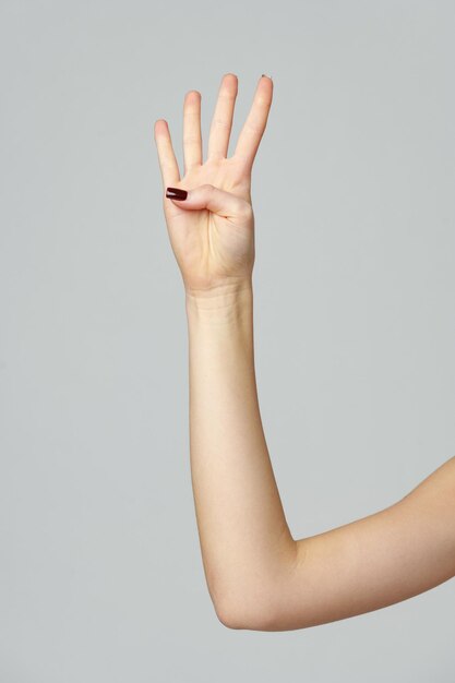 Female hand showing four fingers up on gray background