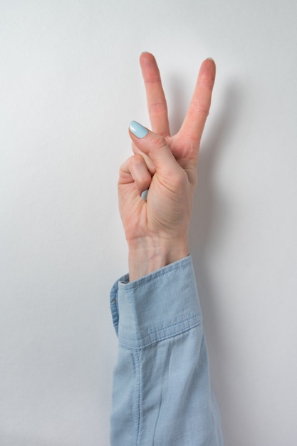 Female hand showing gesture of victory. Two fingers raised up on white wall. Peace and Victory. Vertical frame