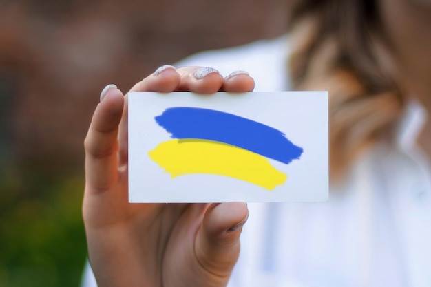 여성의 손은 자연의 배경에 우크라이나의 국기 그림이 있는 명함을 보여줍니다. 우크라이나에서의 비즈니스 및 작업