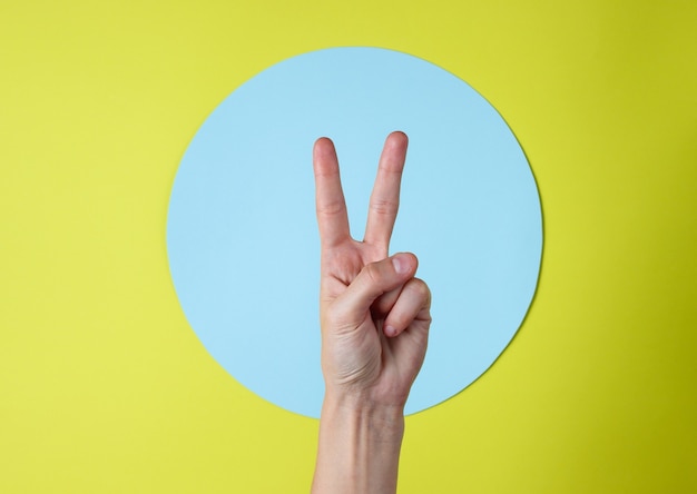 Female hand shows V gesture on a green with a blue circle