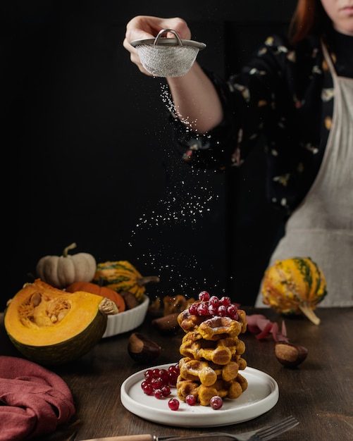 Female hand sieving sugar powder on breakfast waffles and fresh figues