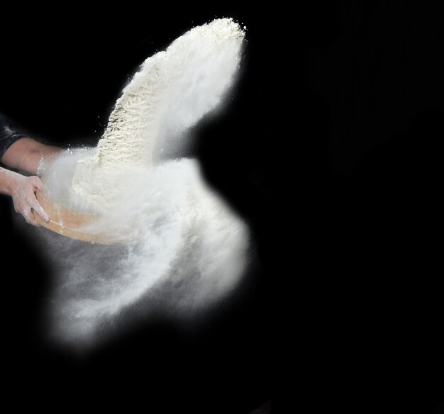 Female hand sifts white wheat flour through a round wooden sieve