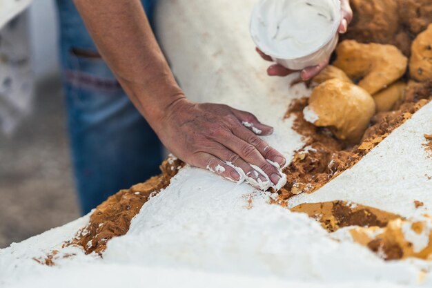 Female hand spreading white paste on the rough surface of a polystyrene figure