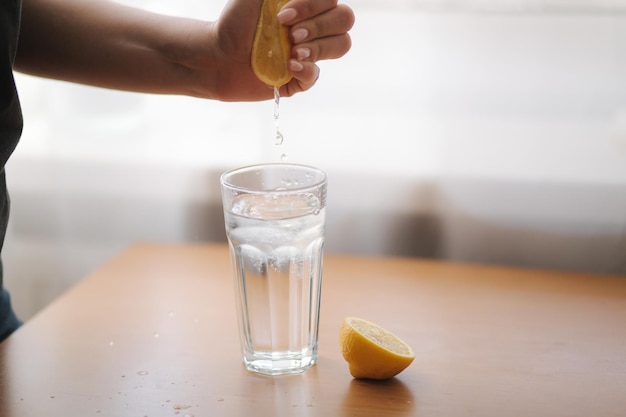 女性の手は、検疫にレモンの新鮮な飲み物を入れた水でグラスにレモン汁を絞ります