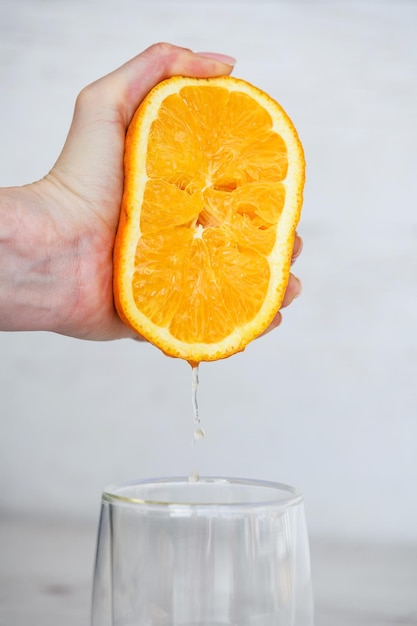 透明なガラスの健康的な朝食の自然な飲み物の下で新鮮な柑橘類のオレンジジュースの半分を絞る女性の手
