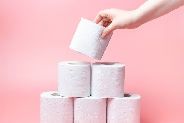 Female hand stacks toilet paper in a stack on pink background close-up.