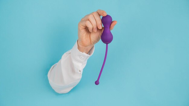 Female hand sticking out of a hole in a blue background and holding a kegel machine