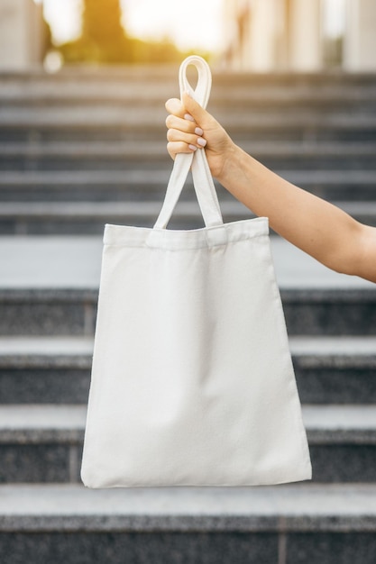 Female hand on the street holding white eco bag mock up