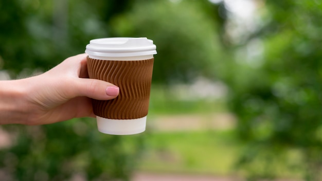 Фото Женская рука взять бумажную чашку кофе, чтобы пойти в парк
