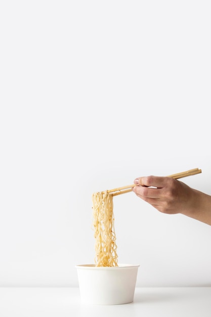 Female hand takes Chinese noodles with Chinese chopsticks from a paper bowl on a white background