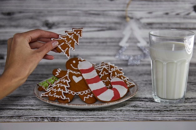 Female hand takes a cookie from plate Glass of milk on wooden vintage table Aesthetic holidays