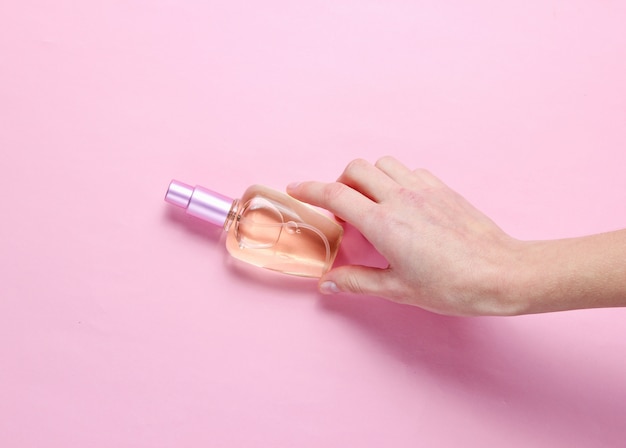 Female hand takes perfume bottle on a pink pastel background. Minimalism. Beauty and fashion concept.