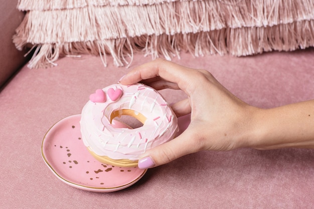 Женская рука берет сладкий розовый пончик на розовом