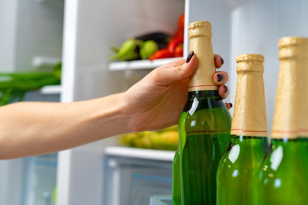 Mano femminile che cattura bottiglia di birra da un frigorifero si chiuda