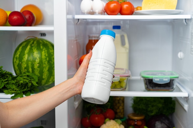 Female hand taking bottle of milk from a fridge close up