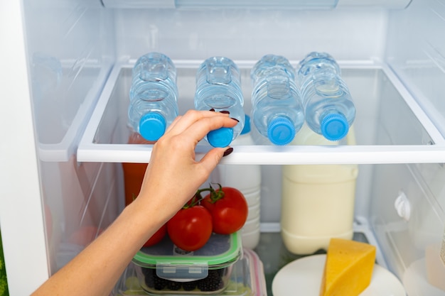 Mano femminile che cattura bottiglia di acqua da un frigorifero